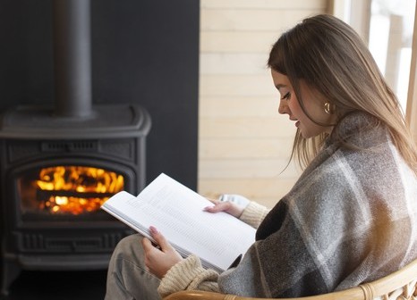 Femme lisant au chaud près d’un poêle à bois